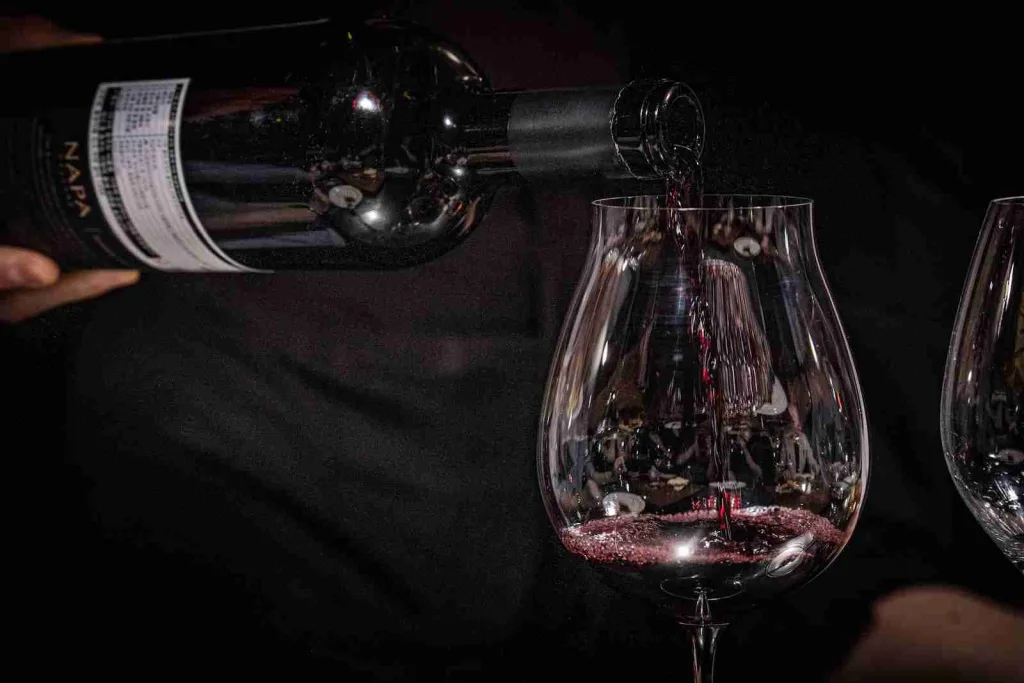 a person pouring red wine into a wine glass
