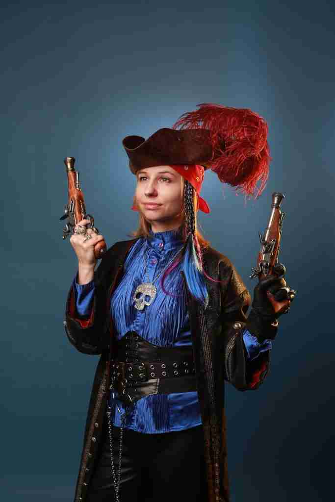 26 Fun Facts About Pirates | Sailing the Seas 2 Young pondering woman in pendant with decorative skull holding retro pistols while looking forward on gray background