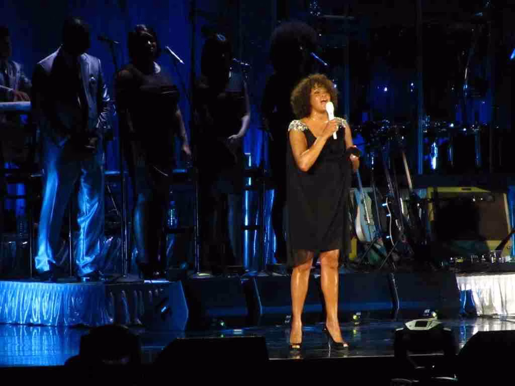 whitney houston on stage wearing black suit and hold a mic