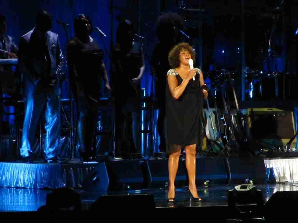 23 Mind-Blowing Fun Facts About Whitney Houston 4 whitney houston on stage wearing black suit and hold a mic