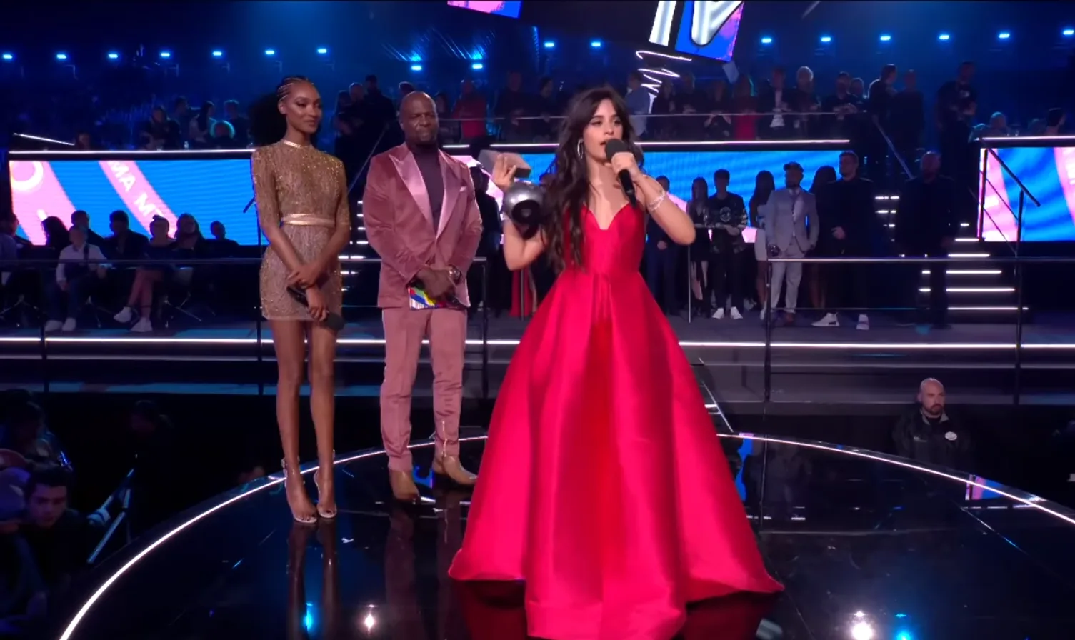 Camila Cabello preforming on stage and some people in back are listening to her, showcasing interesting facts about Camila cabello 